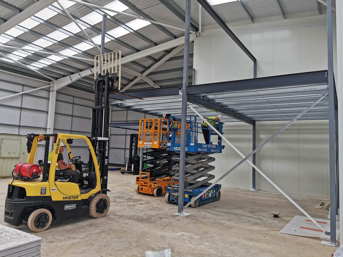 Workers on scissor lifts and forklift inside warehouse assembling metal mezzanine structure