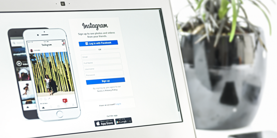 Instagram login page displayed on a laptop screen with two smartphones shown and a plant pot in the background