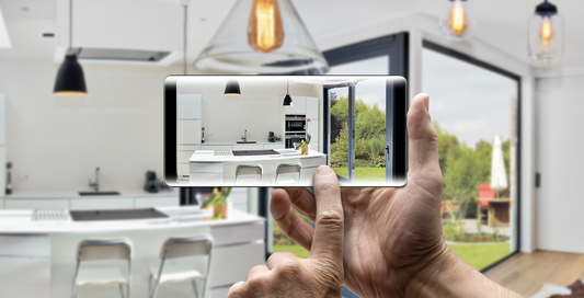 Person using smartphone to photograph a modern white kitchen with island and garden view through glass doors