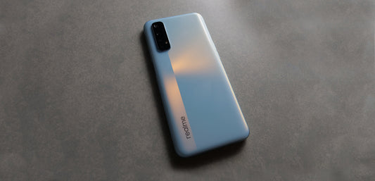 Realme smartphone with triple rear cameras on textured gray surface, sleek silver design