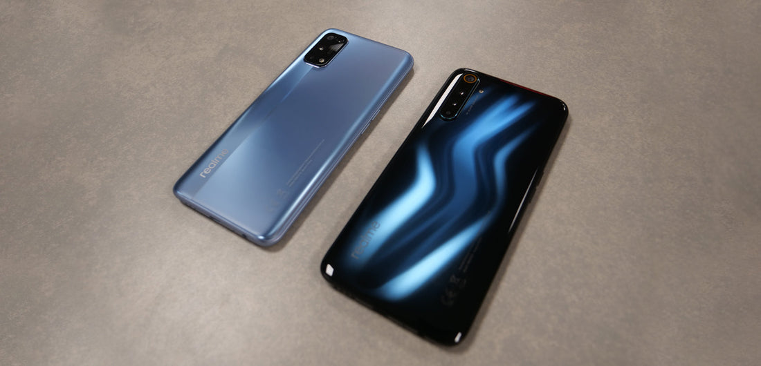 Two Realme smartphones side by side on a table, one matte blue and one glossy black with blue light reflection, highlighting rear cameras