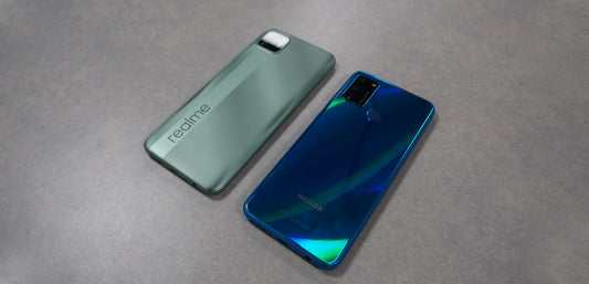 Back view of green realme C11 and blue Honor 9A smartphones on gray surface