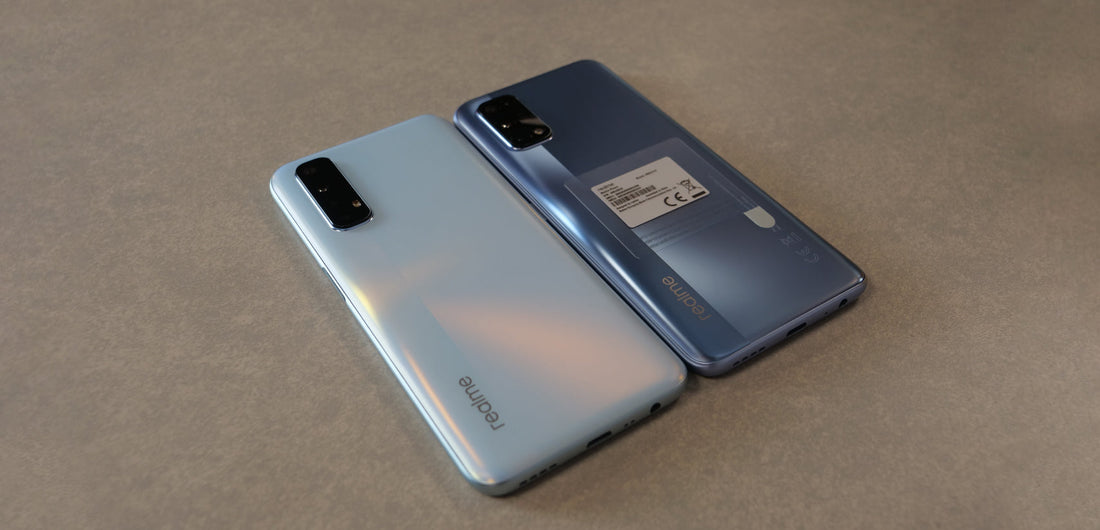 Two Realme smartphones with triple cameras on a grey surface, one silver and one dark blue, showcasing sleek design